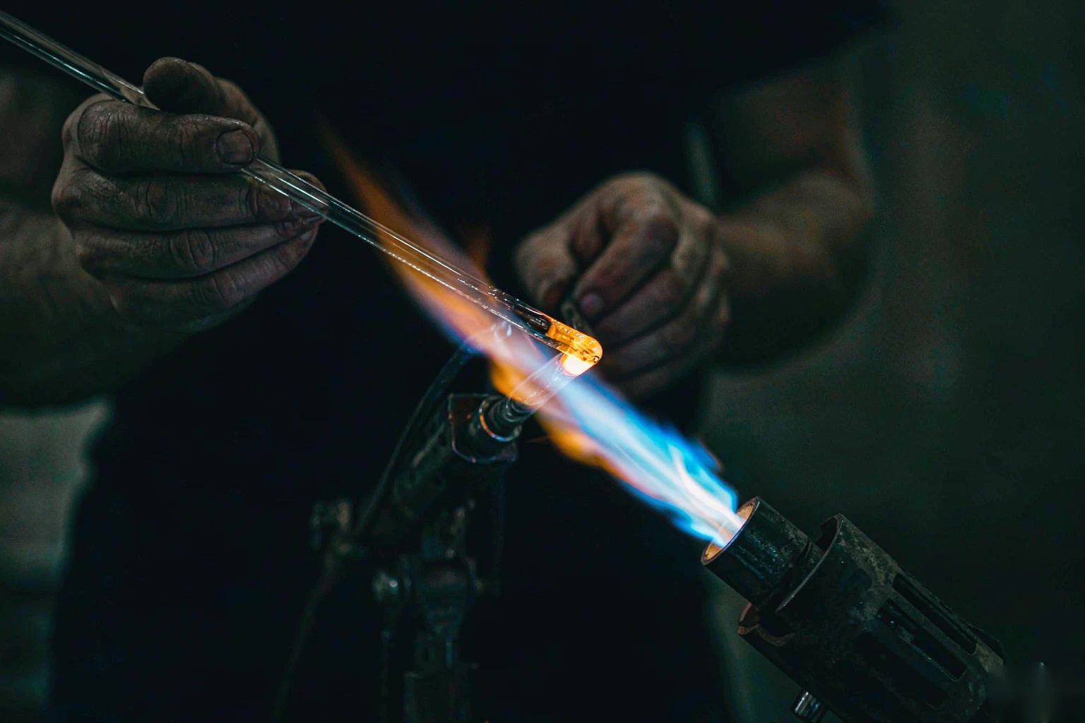 A glassworker melting a rod of glass in a torch flame